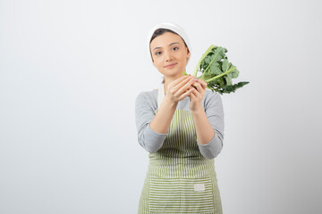 Young beautiful woman in apron holding fresh broccoli on white background