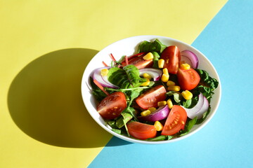 spring salad with tomatoes red onion canned corn and salad greens in white bowl on the yellow and blue background