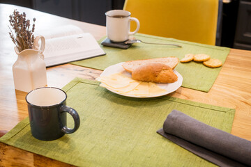 on linen towel on a wooden table, simple breakfast of two mugs of coffee, and slices of bread and cheese