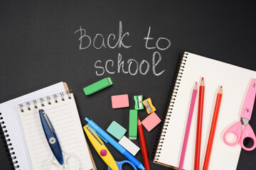 school supplies: multicolored wooden pencils, notebook, pencil sharpener and white chalk inscription back to school