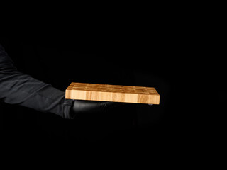 male chef black clothes stands against a black background and holds in his hand a empty rectangular...