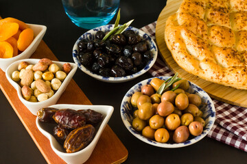 Ramadan beginning meal is with sweet dry dates,apricot,black olives,water and Ramadan bread on black surface.