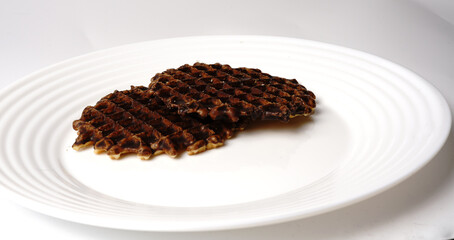 Sweet waffles poured with chocolate on a white plate on a white background.
