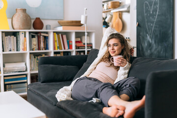 Obraz premium woman relaxing on sofa at her home. she is drinking morning coffee