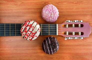 Artistic food composition of donuts on top of a acoustic guitar. Top view. Colorful cakes with sprinkles. Wood background.