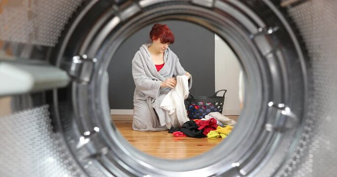 Woman sorting dirty clothes before washing. Housewife sitting with basket and sorting just drying clothes. View Looking Out From Inside Washing Machine.