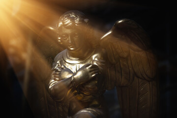 Ancient statue of gold angel praying in the sunlight.
