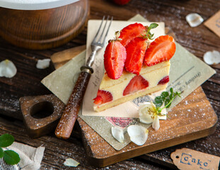 tasty homemade strawberry cake fraisier with biscuits and lot of white cream on wooden cake stand on rustic table with flowers, vintage forks, copper cups