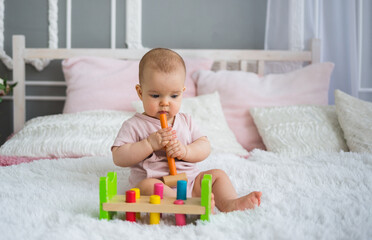 Naklejka premium a beautiful baby girl in a pink bodysuit sits on the bed and plays with an educational toy