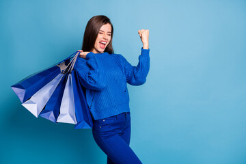Photo of crazy excited girl hold bags raise fists with shopping bags isolated over blue color...