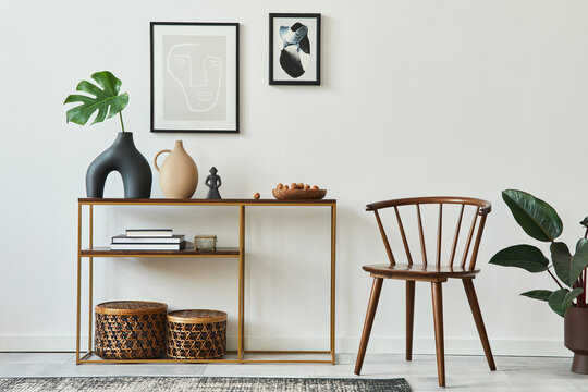 Stylish concept of living room interior with mock up poster frames, wooden console, chair, tropical leaf in vase, rattan baskets, plant, carpet and personal accessories in home decor. Template.