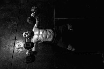 Young sweaty strong muscular fit man with big muscles doing bench press with heavy dumbbell weights...