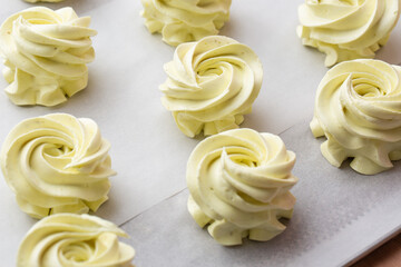 Many sweet handmade zephyrs or marshmallows drying on baking sheet covered with white parchment. Cooking concept. Isolated close-up of white marshmallows, meringues, zephyrs. Sweet delicious desserts.