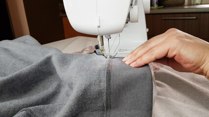 a seamstress works on a sewing machine. women's hands hold the gray fabric and make a straight stitch on it.