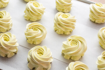 Many sweet handmade zephyrs or marshmallows drying on baking sheet covered with white parchment. Cooking concept. Isolated close-up of white marshmallows, meringues, zephyrs. Sweet delicious desserts.