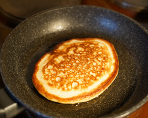 A golden-colored pancake is fried in a frying pan at home. Breakfast