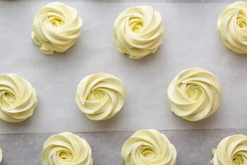 Many sweet handmade zephyrs or marshmallows drying on baking sheet covered with white parchment. Cooking concept. Isolated close-up of white marshmallows, meringues, zephyrs. Sweet delicious desserts.