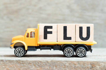 Toy truck hold alphabet letter block in word flu on wood background