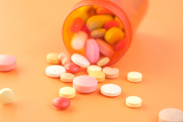 Close up of many colorful pills and capsules spilling on orange background 