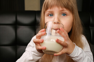 The girl drinks milk with cookies in the morning at breakfast.