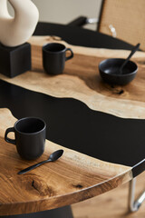 Fototapeta na wymiar Minimalist composition on the design wooden and epoxy table with black teapot, cups and spoon. Modern dining room interior. Details. Template...