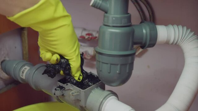 Clearing a blockage in the plumbing check valve in the kitchen, A hand in a yellow glove takes out the trash.