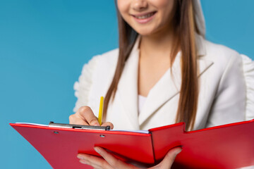 Cropped image of smiling young woman, trainer,student, business woman, consultant isolated on a blue background, writing pencil notes in work folder. Good job concept.