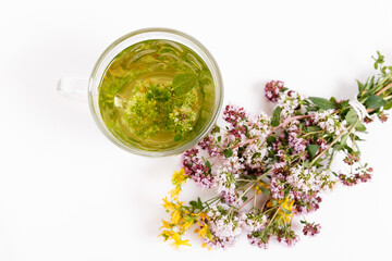 Glass cup of herbal tea with dry oregano flowers on white table background with copy space. Top view. Selective focus