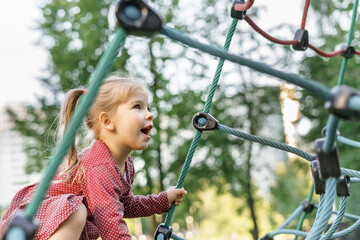 Children play and climb outdoors on a sunny summer day. Nice kid girl on a swing nest in a preschool sports complex.