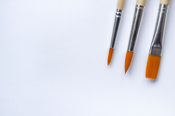 Bristle brushes for coloring and painting with paints with copy space. Tassels for paints on a white paper background close-up with a place for the text.