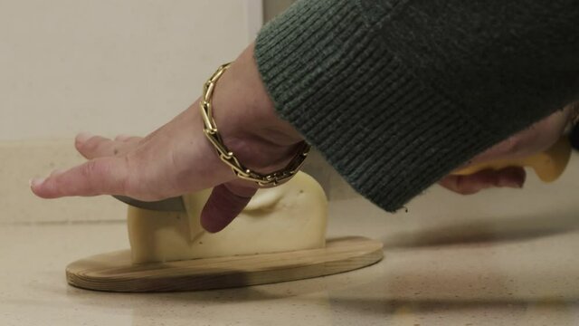 Galician tetilla cheese is cut with a knife by a woman's hands in a kitchen.