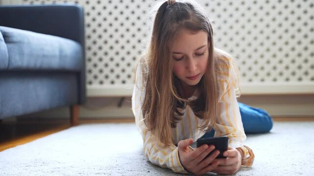 Tween girl with smartphone lying on the carpet.