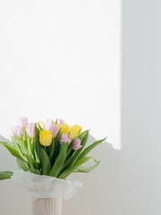 Fresh spring bouquet of colored tulips in eco packaging on the background of a white textured wall in a stylish vase. Copy space.