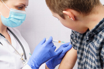 The doctor injects the vaccine into the boy's hand. Vaccination against coronavirus. The doctor vaccinates the child. boy gets a flu shot.