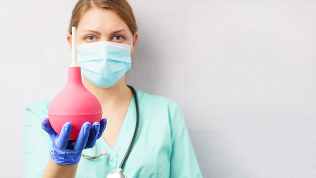 nurse doctor with enema in hand. a woman in a medical uniform and a protective mask holds an enema.