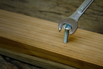 Close-up wrench screwing nut a furniture screw into a wooden plank, The effort  wrong of tools as a fail concept