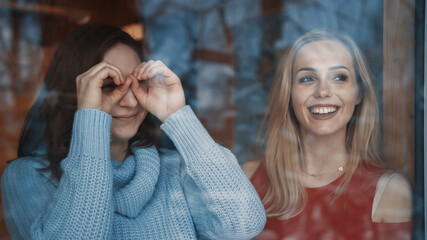 Young girls friends enjoying winter vacation. Looking through the window on snow covered neighborhood . High quality photo