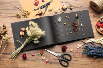 Flat lay composition with beautiful dry flowers and herbarium album on wooden table