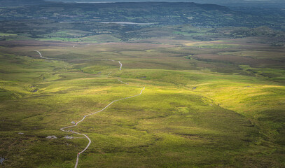 Drone or aerial view on winding wooden path and boardwalk between green fields illuminated by sunlight in Cuilcagh Mountain Park, Northern Ireland