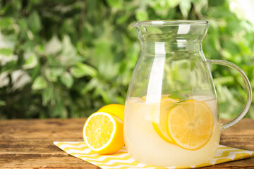 Cool freshly made lemonade in glass pitcher on wooden table. Space for text