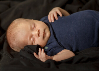 a newborn baby sleeps, Blonde with light skin on a dark background. large portrait, face.