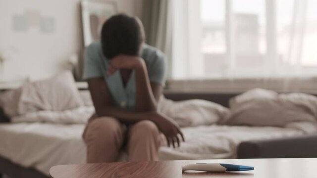 Lockdown of unrecognizable African-American woman sitting on bed in bedroom and crying because of negative pregnancy test result