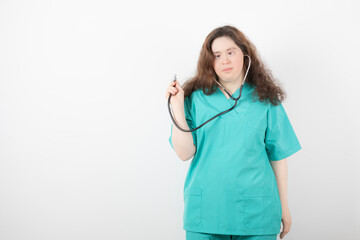 Young female doctor with down syndrome using stethoscope over white wall