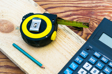 construction meter-tape measure calculator for calculations pencil and wooden board are on the...