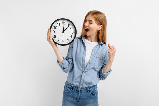 young woman holding round clock making winner gesture, over white background