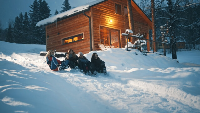 Best friends sliding on the sleds downhill in front of the wooden house. Winter season, Christmas holidays. High quality photo