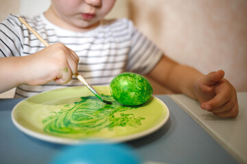 little cute blue-eyed girl in bunny ears paints Easter eggs