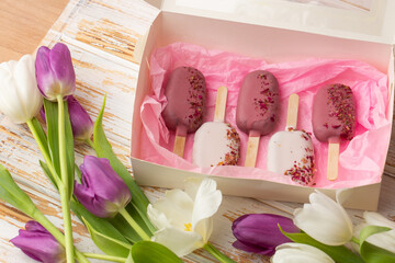 Delicious handmade ice-cream in a gift box isolated on wooden background with white and purple tulips. Sweet present, beautiful flowers, pink colors, flatlay. International women's day, birthday.