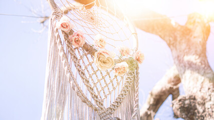 white Dreamcatcher hanging on a tree in beams of the sunset sun. knitting, handmade, wedding, decor