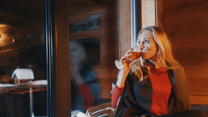 Young woman drinking hot tea with lemon from the wine glass. Sitting near the window and looking at snowfall. High quality photo